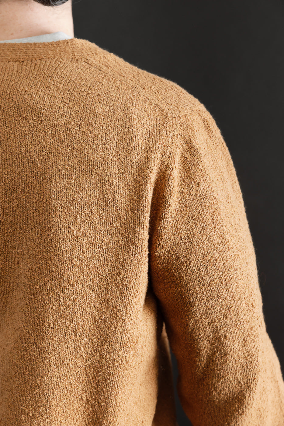 Close-up of the back and shoulder texture on an ochre boucle cardigan worn by a male model, focusing on fabric detail.