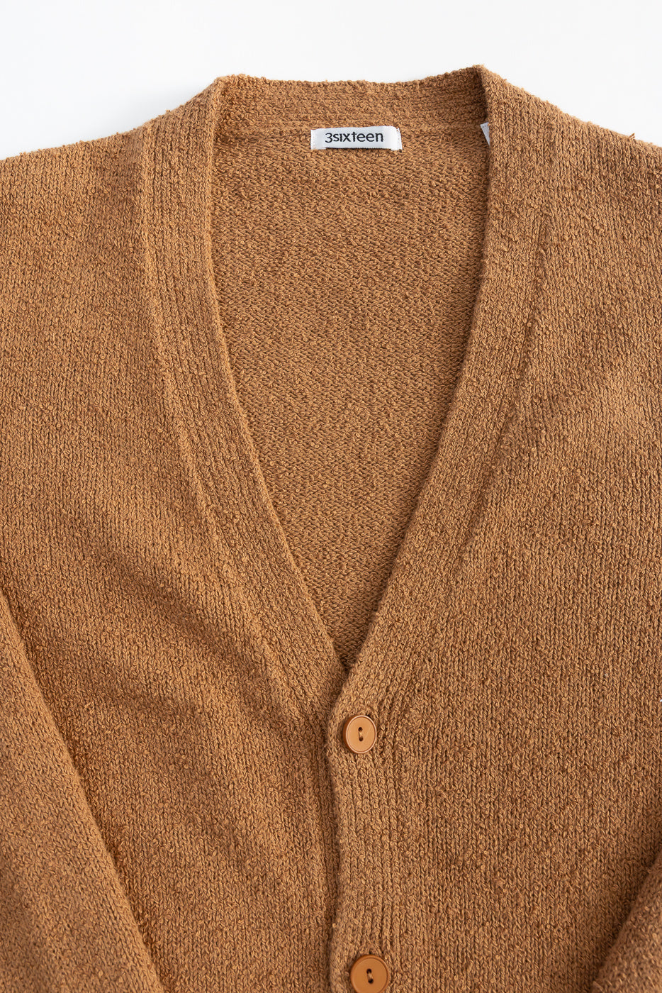 Close-up of the front upper section of an ochre boucle knit cardigan showing V-neck, buttons, and textured fabric.