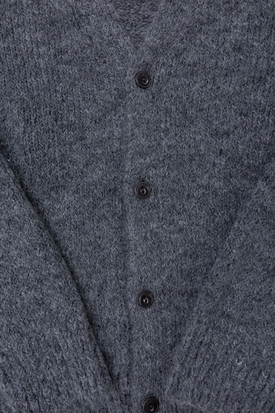 Close-up of the front of a grey knit cardigan showing textured fabric and dark buttons.