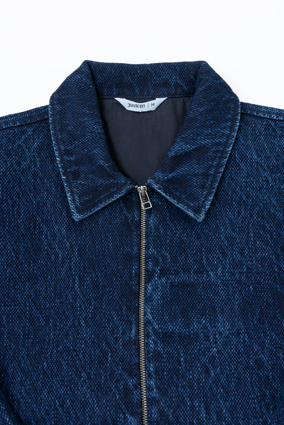 Close-up front view of a blue textured zip-up jacket showing the collar and metal zipper.