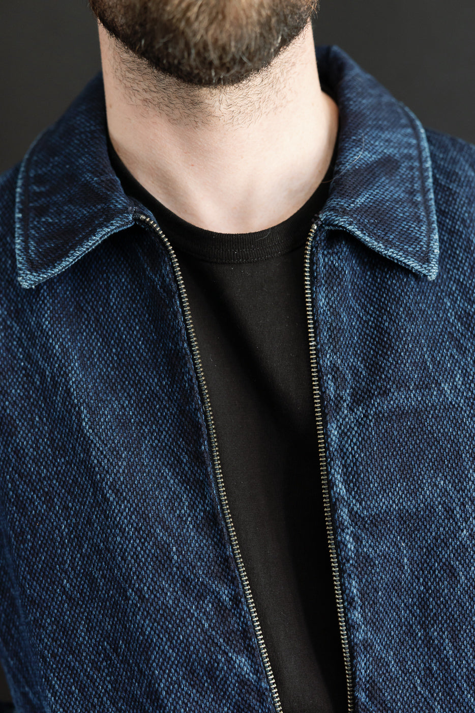Close-up front view of a blue denim jacket's zipper and collar on a male model.