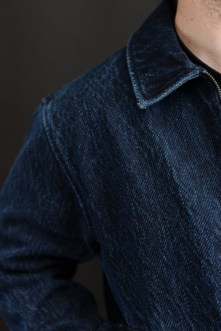 Close-up of the front collar and textured dark blue denim fabric of a jacket.