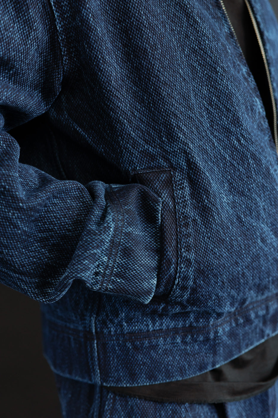Close-up side view of a male model's blue denim jacket showing the pocket and sleeve texture.