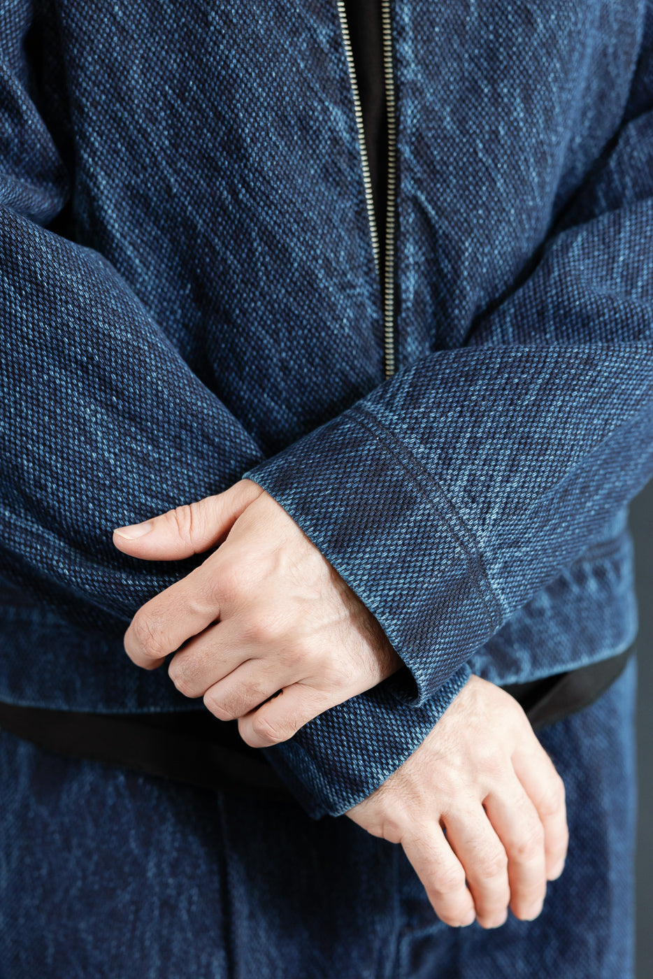 Close-up of the front sleeve and cuff of a blue textured denim jacket on a male model.
