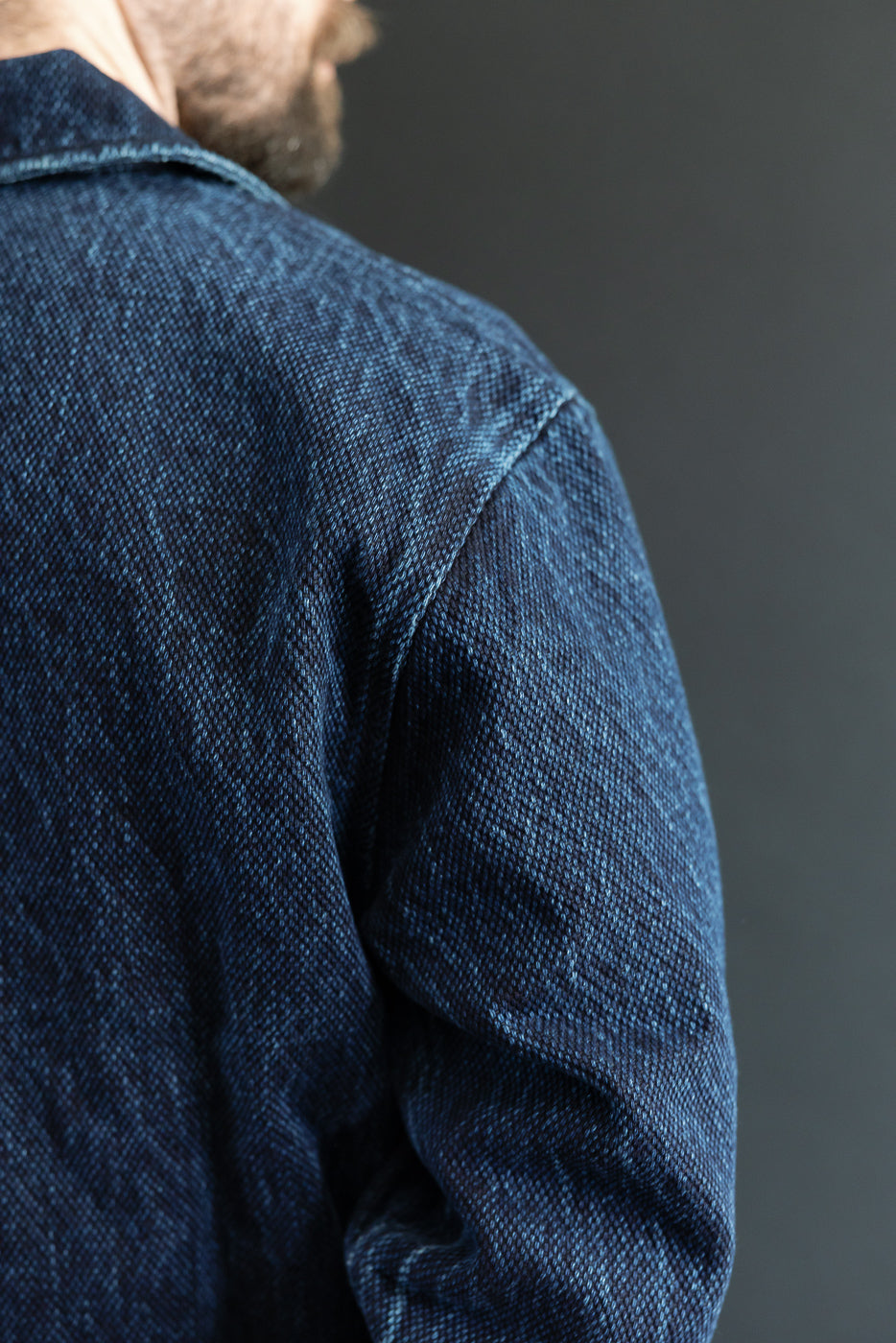 Close-up of the back and right shoulder of a blue denim jacket showing heavy fabric texture.
