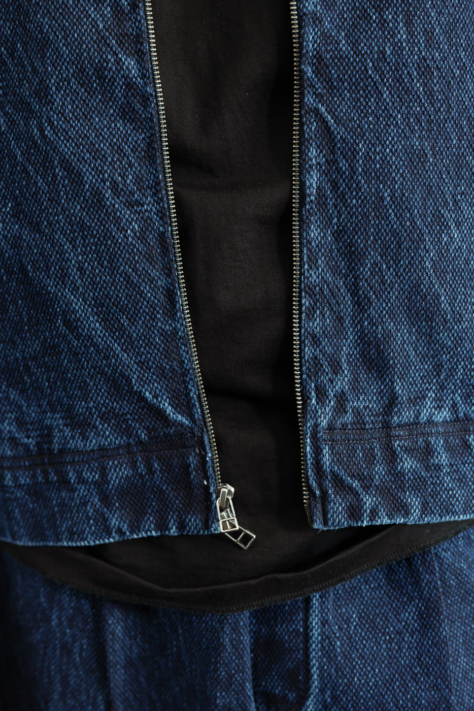 Close-up front view of a blue denim vest showing the silver metal zipper and fabric texture.