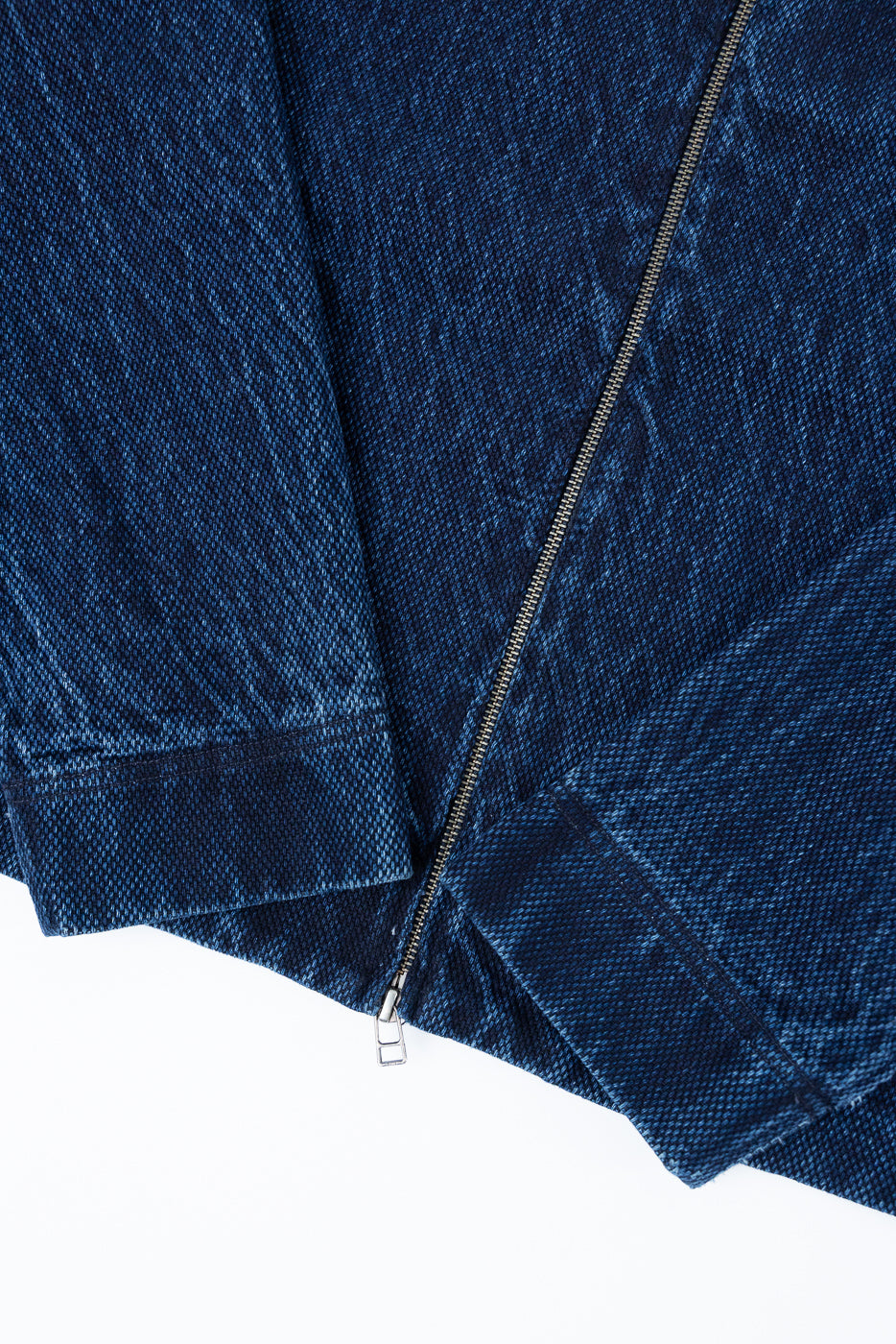 Close-up of the front bottom hem and silver metal zipper on a blue textured denim jacket.