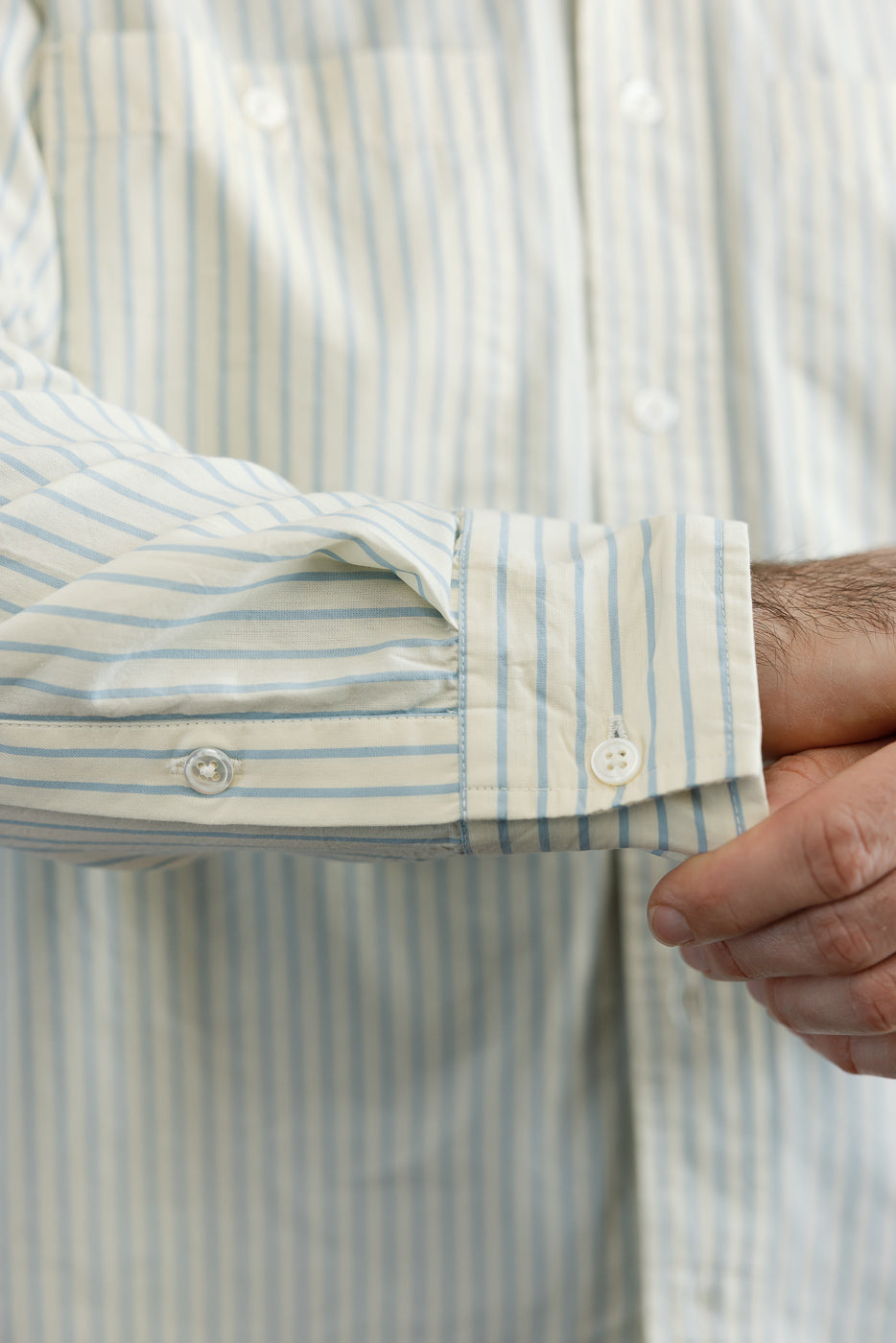 Close-up of the left cuff and button detail on a light blue striped button-down shirt.
