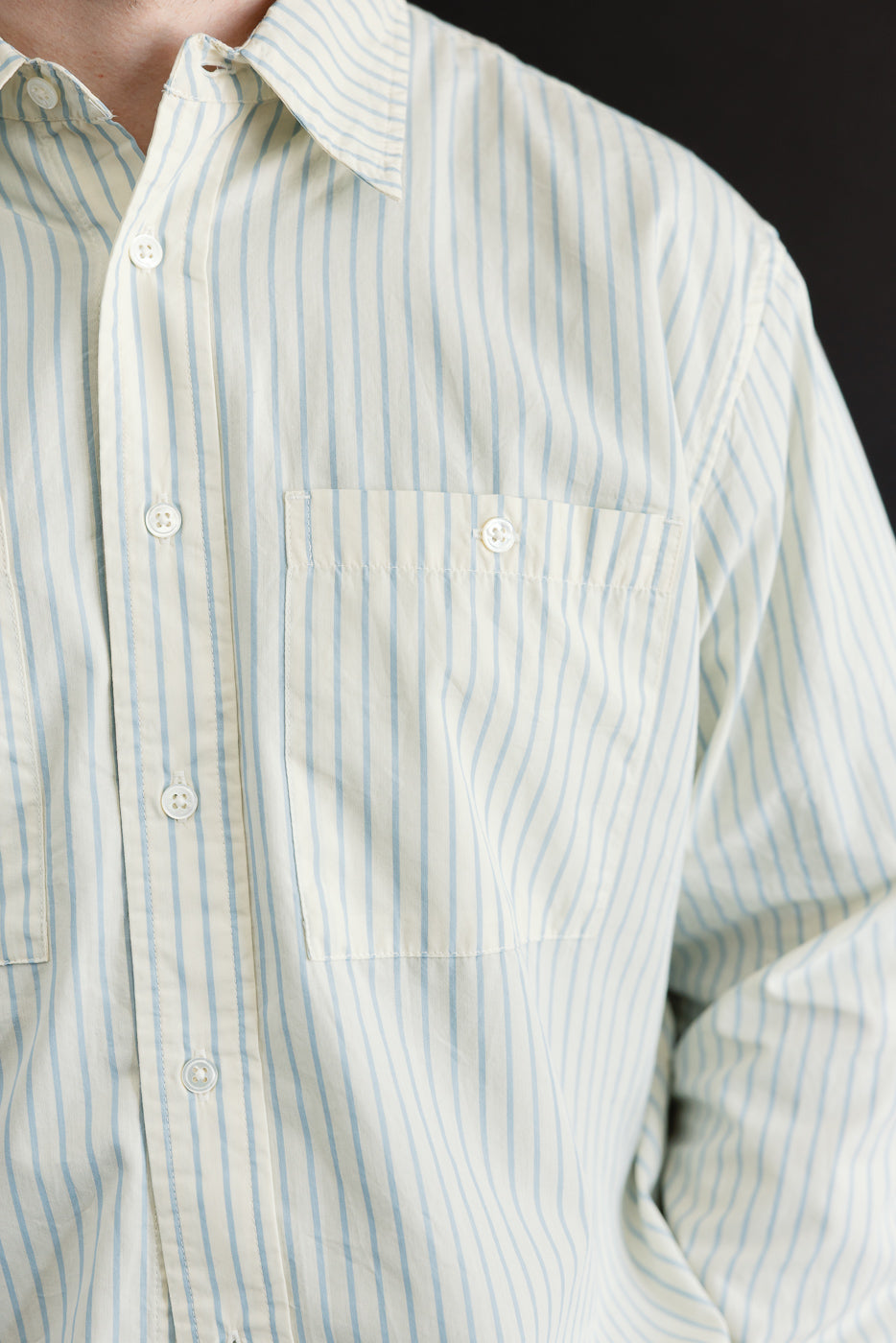 Close-up front view of a light blue striped button-down shirt showing chest pocket and fabric texture.