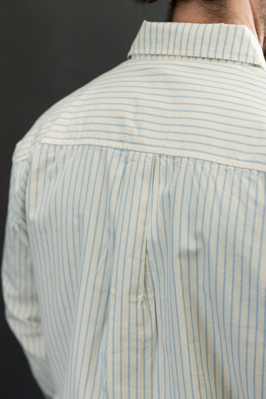 Back view close-up of a blue striped button-down shirt on a male model, 5'9