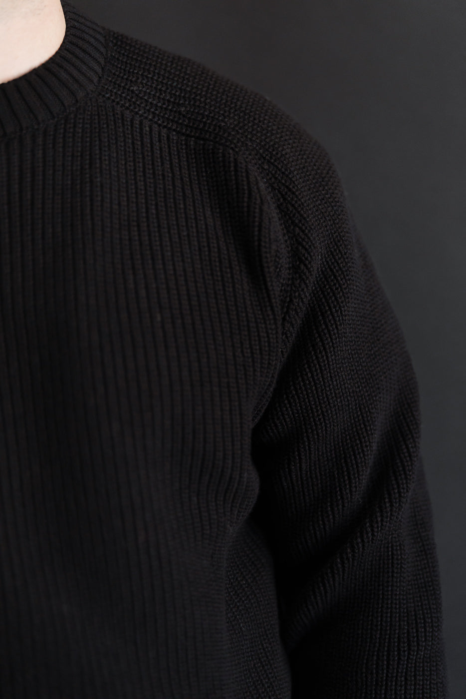 Close-up of the left shoulder and sleeve detail of a black ribbed knit sweater.