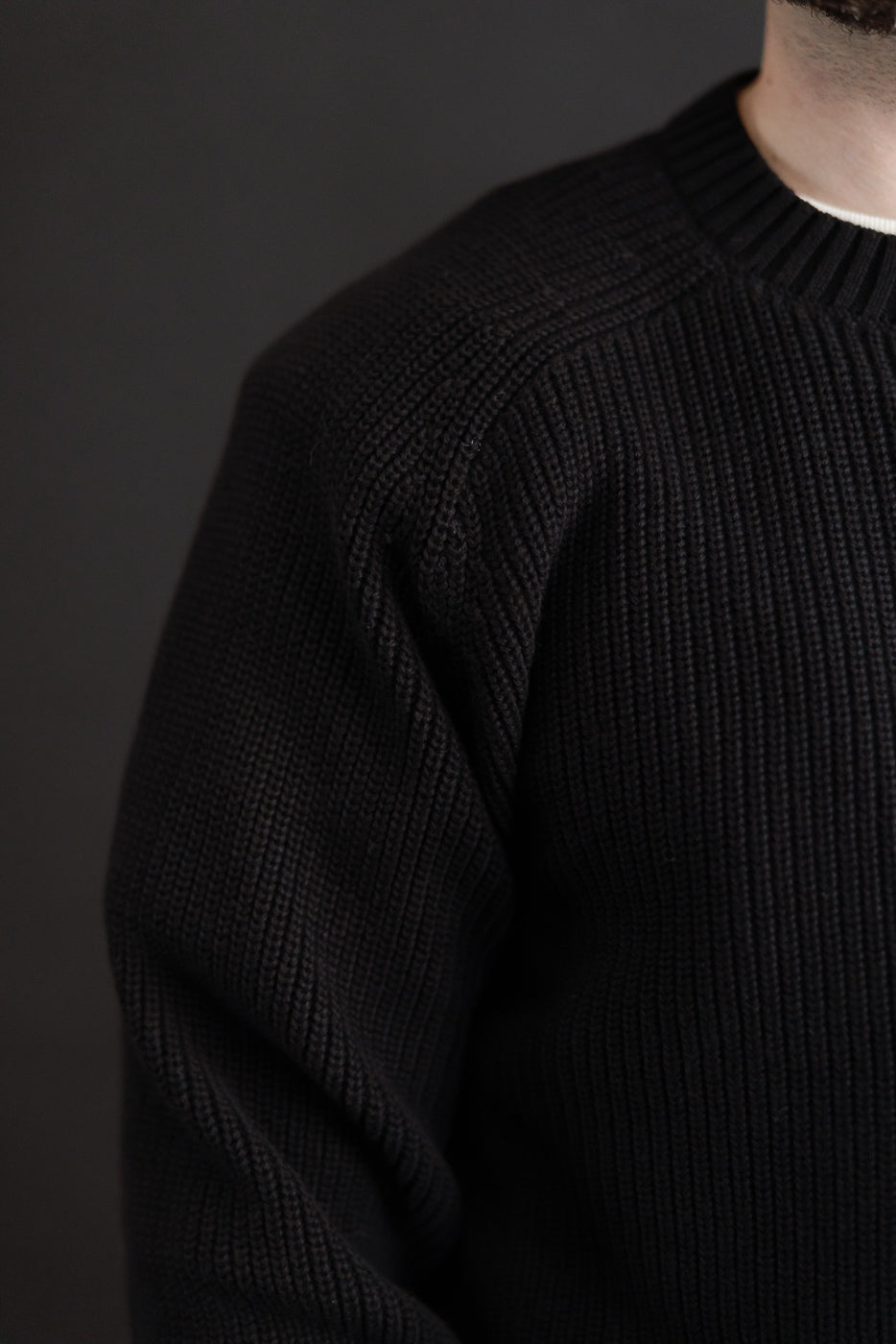 Close-up of the right side and sleeve of a black ribbed knit sweater on a male model.