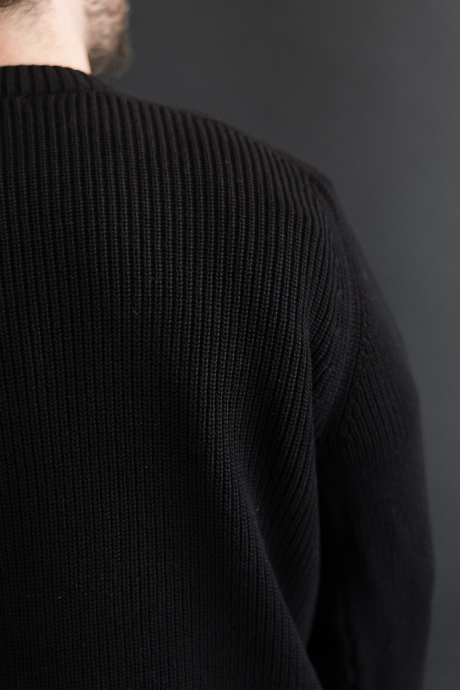 Close-up of the back view of a black ribbed knit sweater, showing vertical texture.