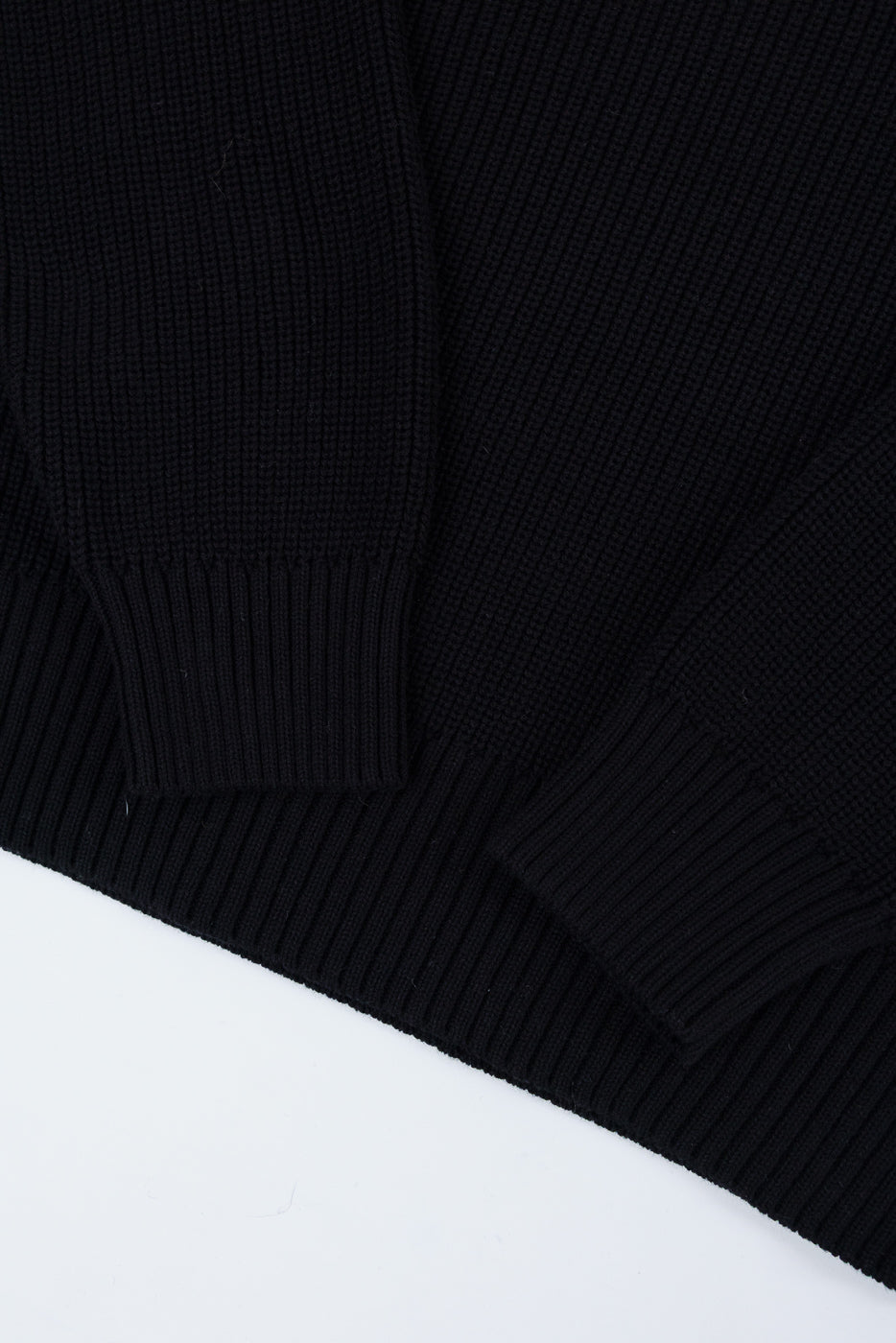 Close-up of the ribbed sleeve cuff and hem of a black knit sweater.