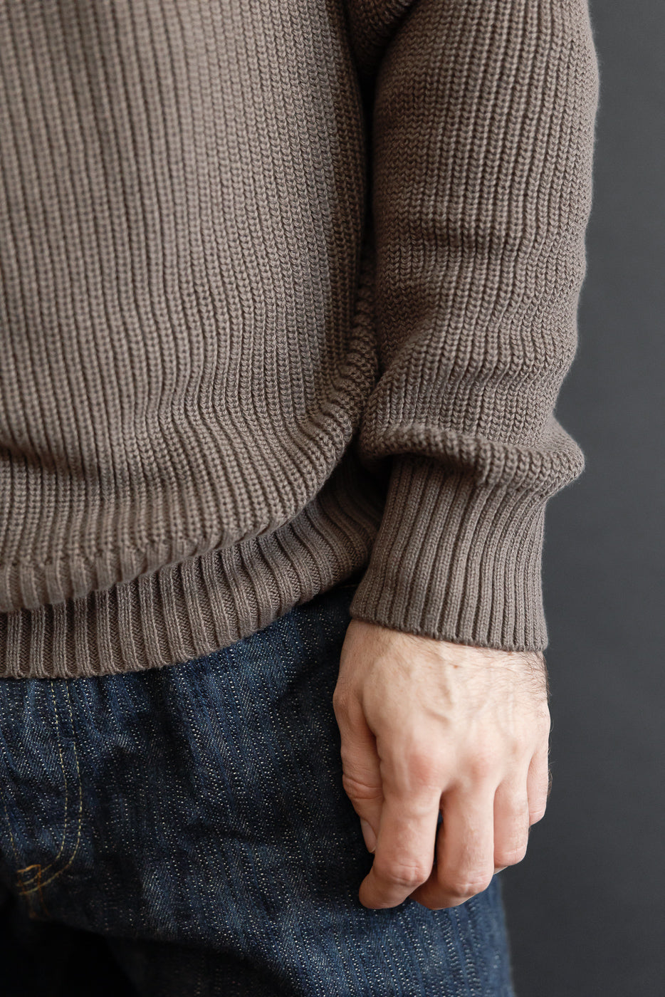 Close-up of the front side of a brown ribbed knit sweater and dark selvedge denim jeans.