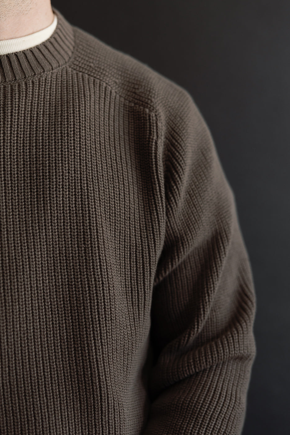 Close-up of the front texture and ribbed collar of a brown knit sweater worn by a male model.