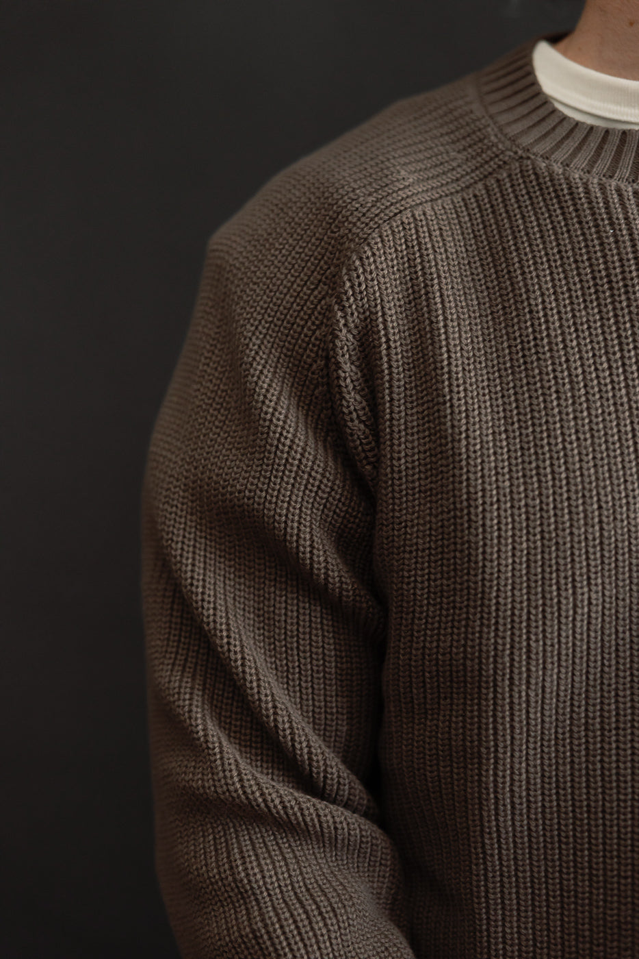 Close-up of the front and side of a male model's brown textured knit crewneck sweater.