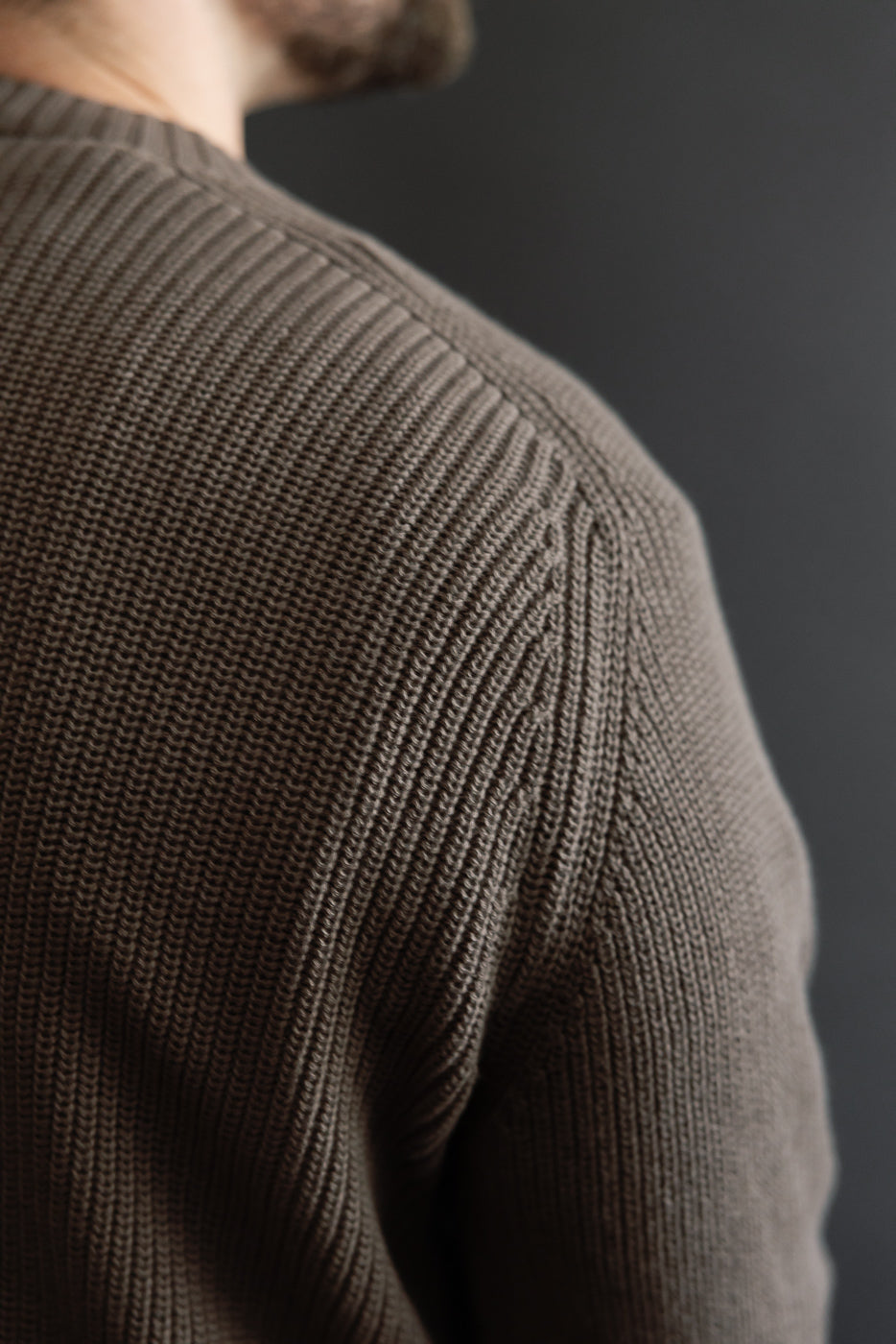 Close-up of the back shoulder and sleeve texture of a brown ribbed knit sweater.