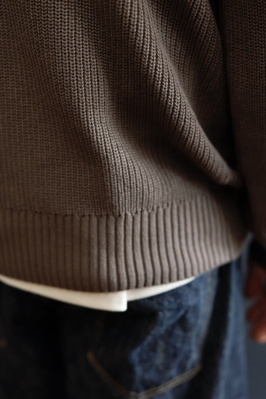 Close-up of the ribbed hem and knit texture on the bottom front of a brown sweater.