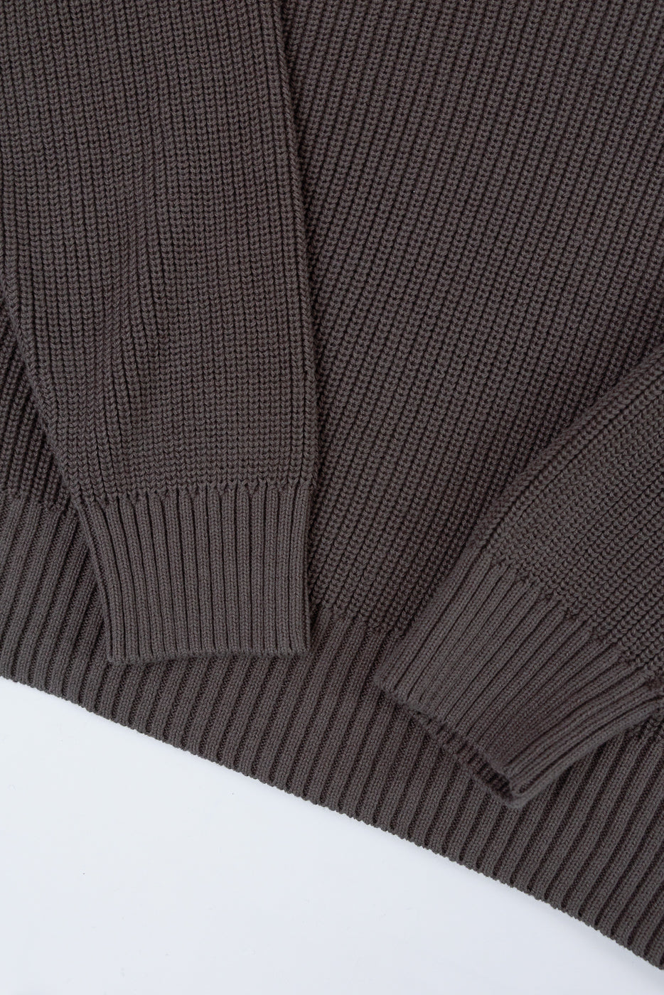 Close-up of the ribbed cuff and textured knit fabric on the front of a dark brown sweater.