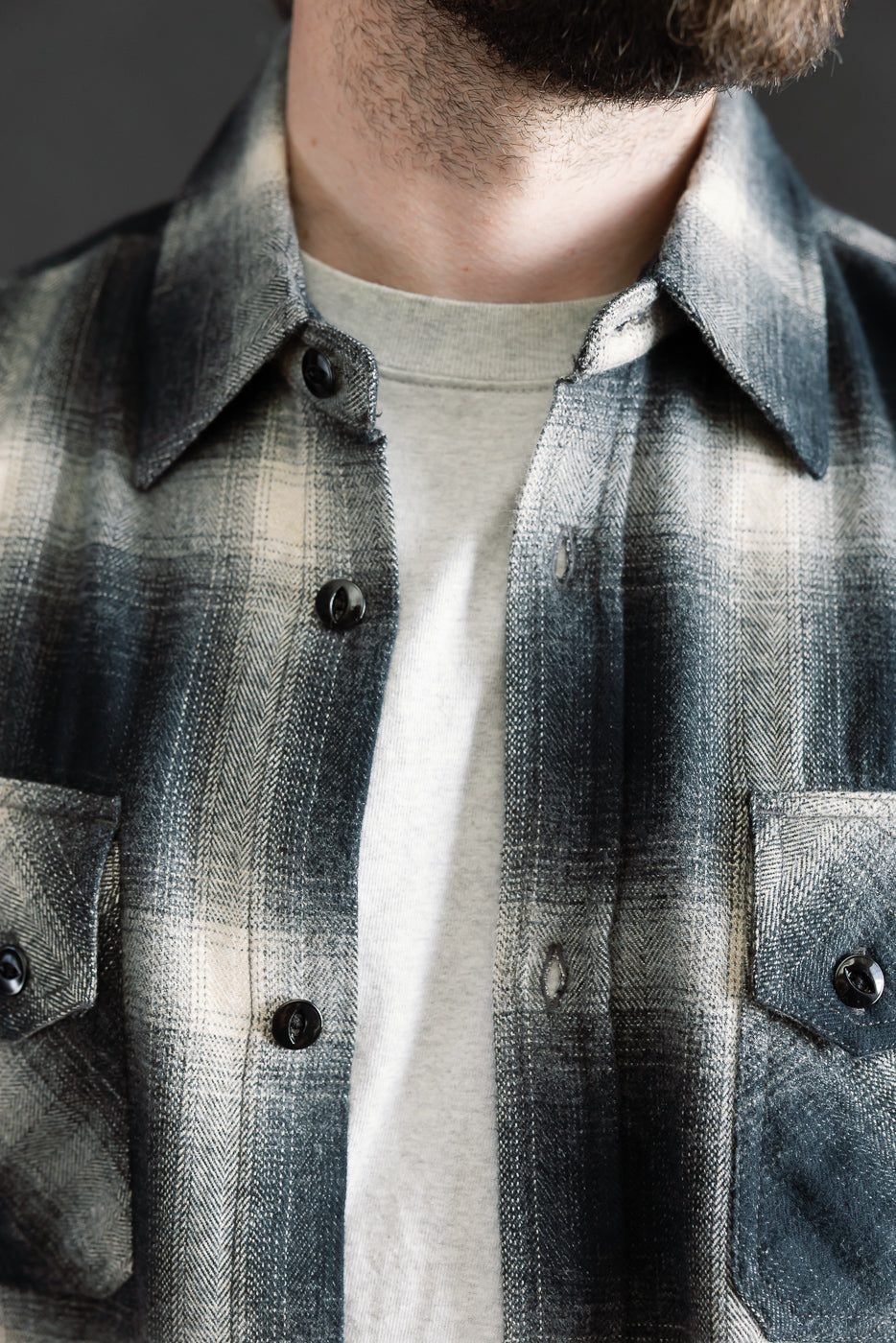 Close-up front view of black ombre plaid flannel shirt on male model, showing collar, buttons, and chest pockets. Model is 5'9
