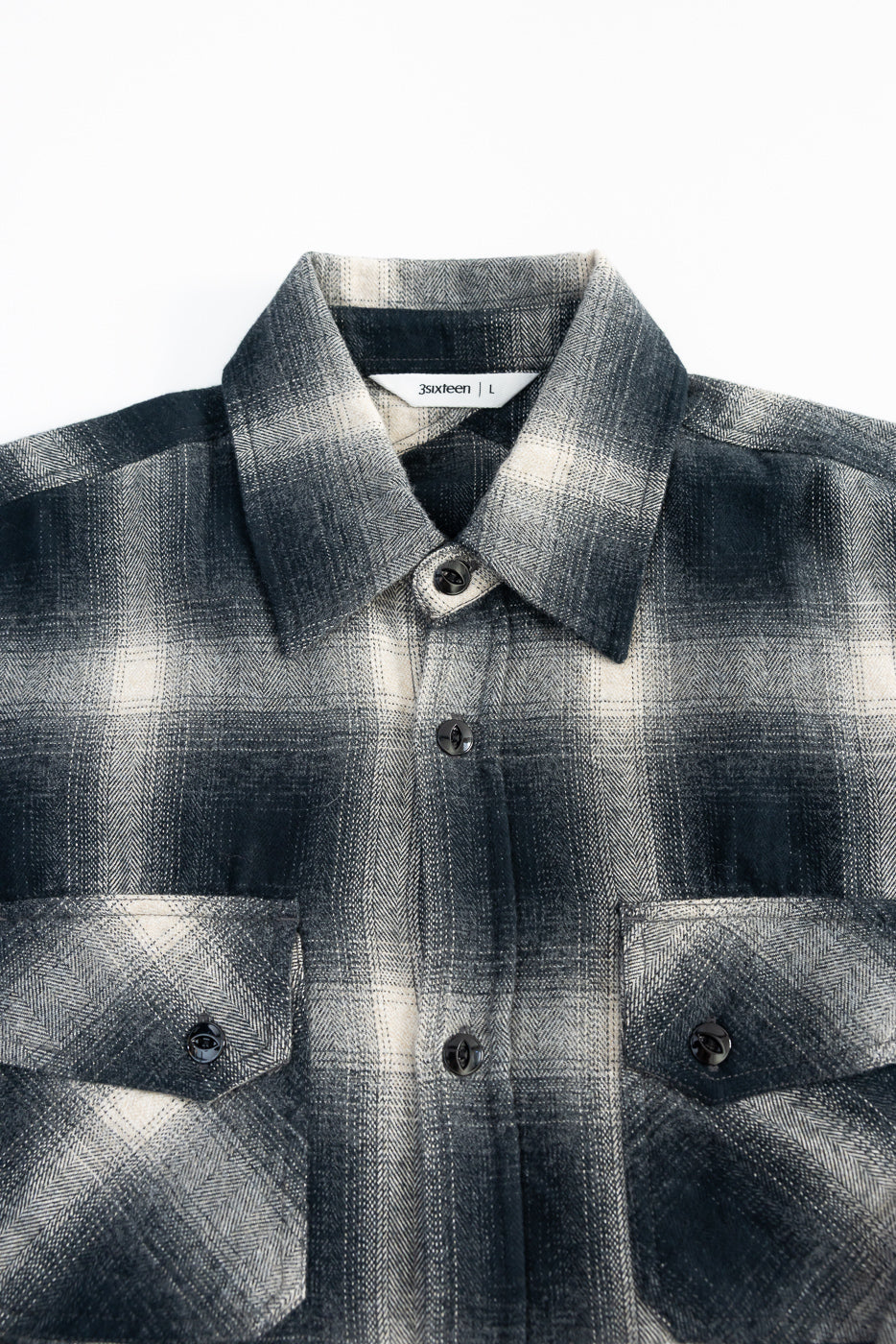 Close-up front view of black ombre plaid flannel shirt, showing collar, chest pockets, and button details.