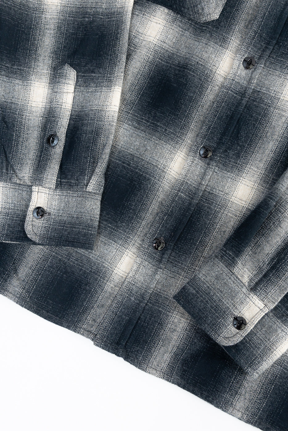 Close-up of front lower section of black ombre plaid flannel shirt showing cuff buttons, pocket flap, and soft textured fabric.