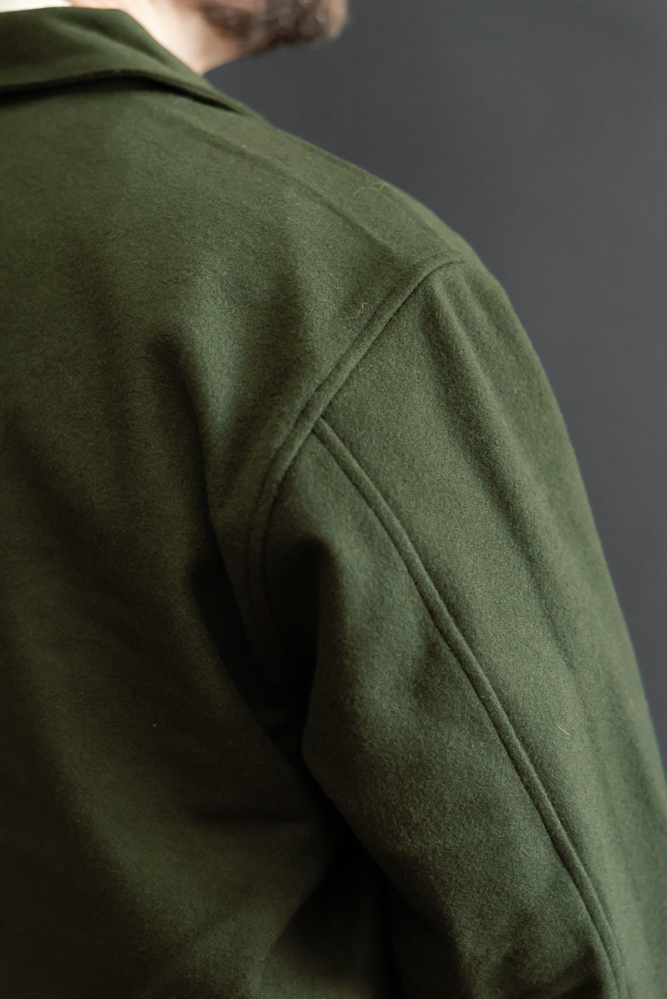 Close-up of the back and right shoulder of a green wool jacket showing fabric texture.
