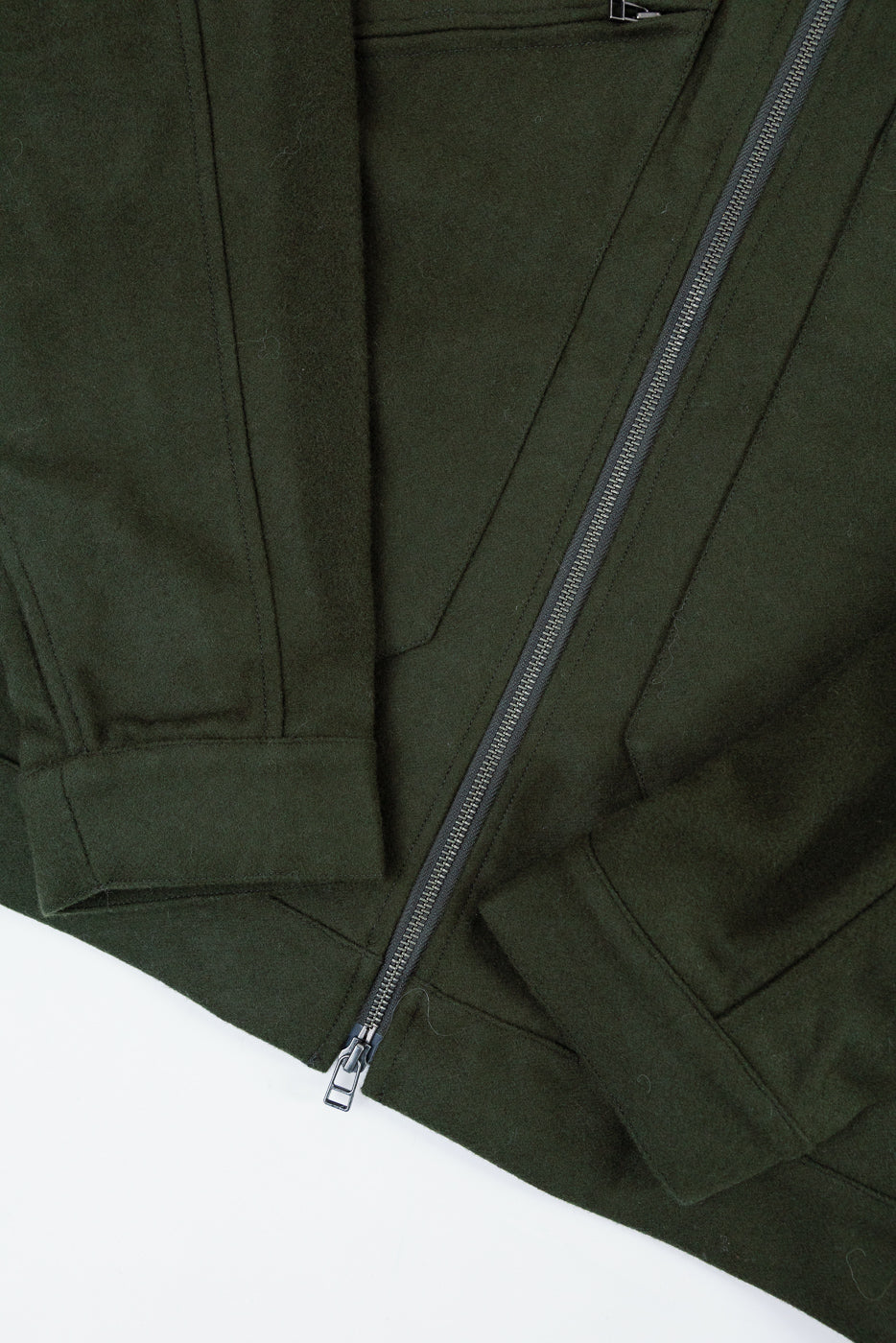 Close-up of the front right side of a dark green wool jacket showing the zipper and fabric texture.