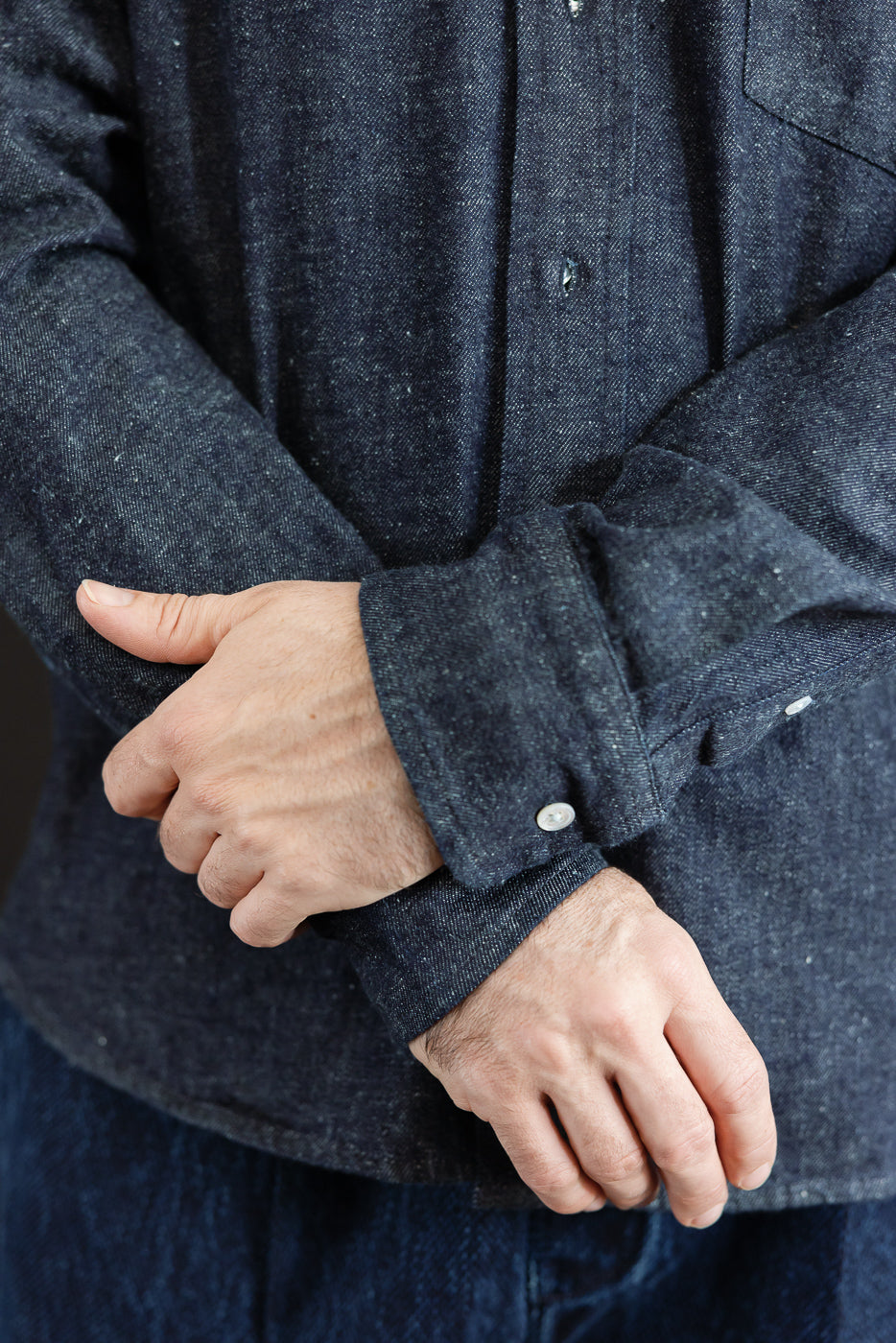 Close-up of the cuff and sleeve detail of a dark blue textured denim shirt on a male model.
