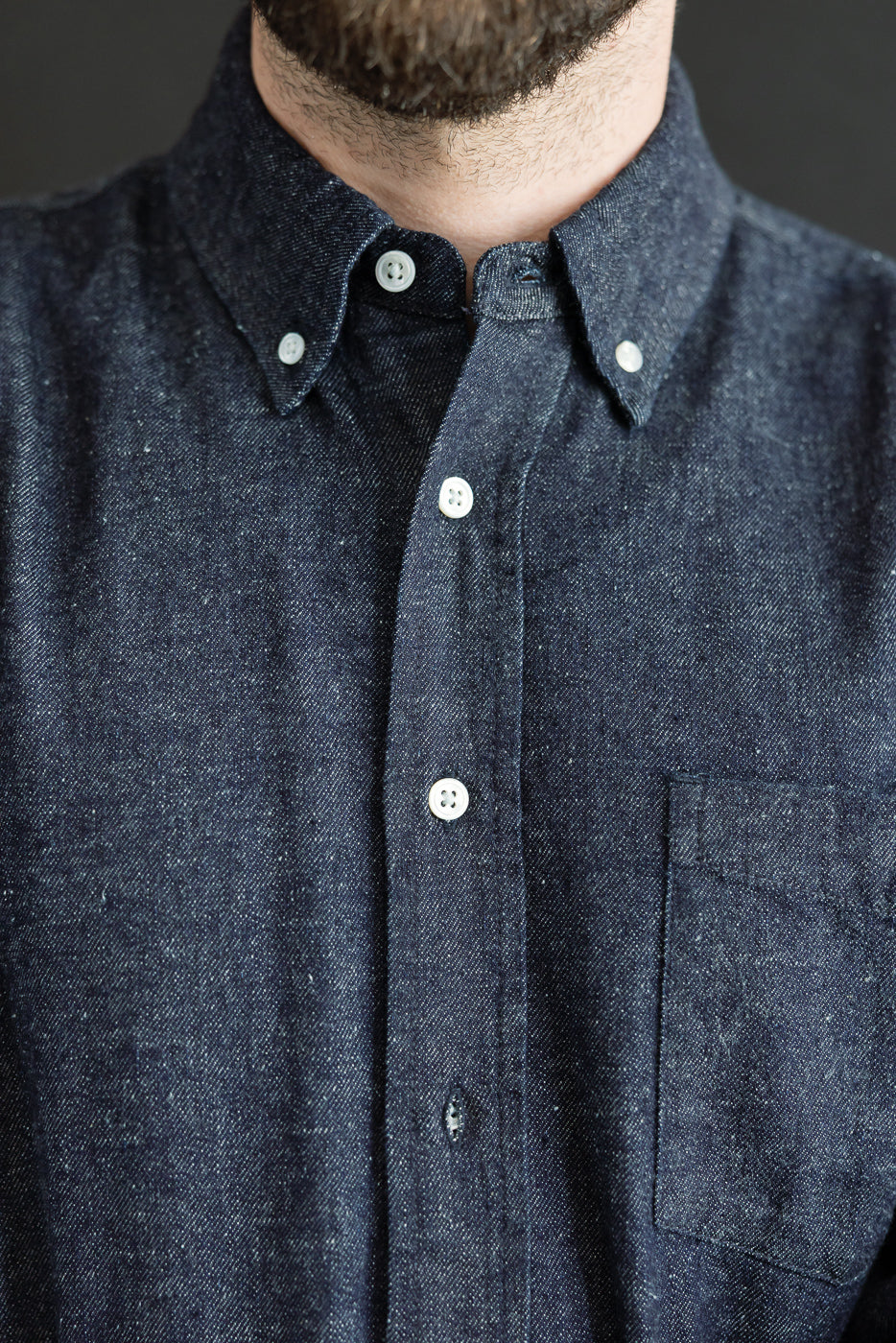Close-up front view of a navy denim button-down shirt showing collar, buttons, and fabric texture.