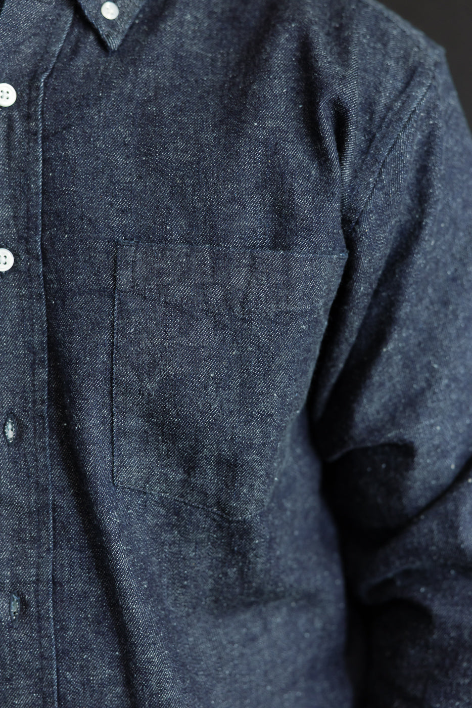 Close-up of the front left chest pocket and fabric texture of a navy blue denim shirt.