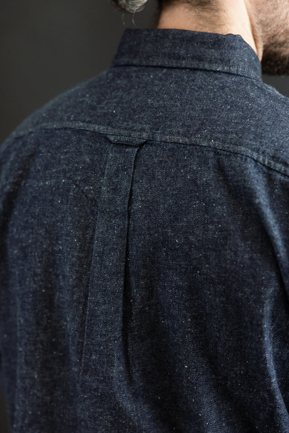 Close-up back view of a dark indigo denim shirt showing fabric texture and yoke detail.