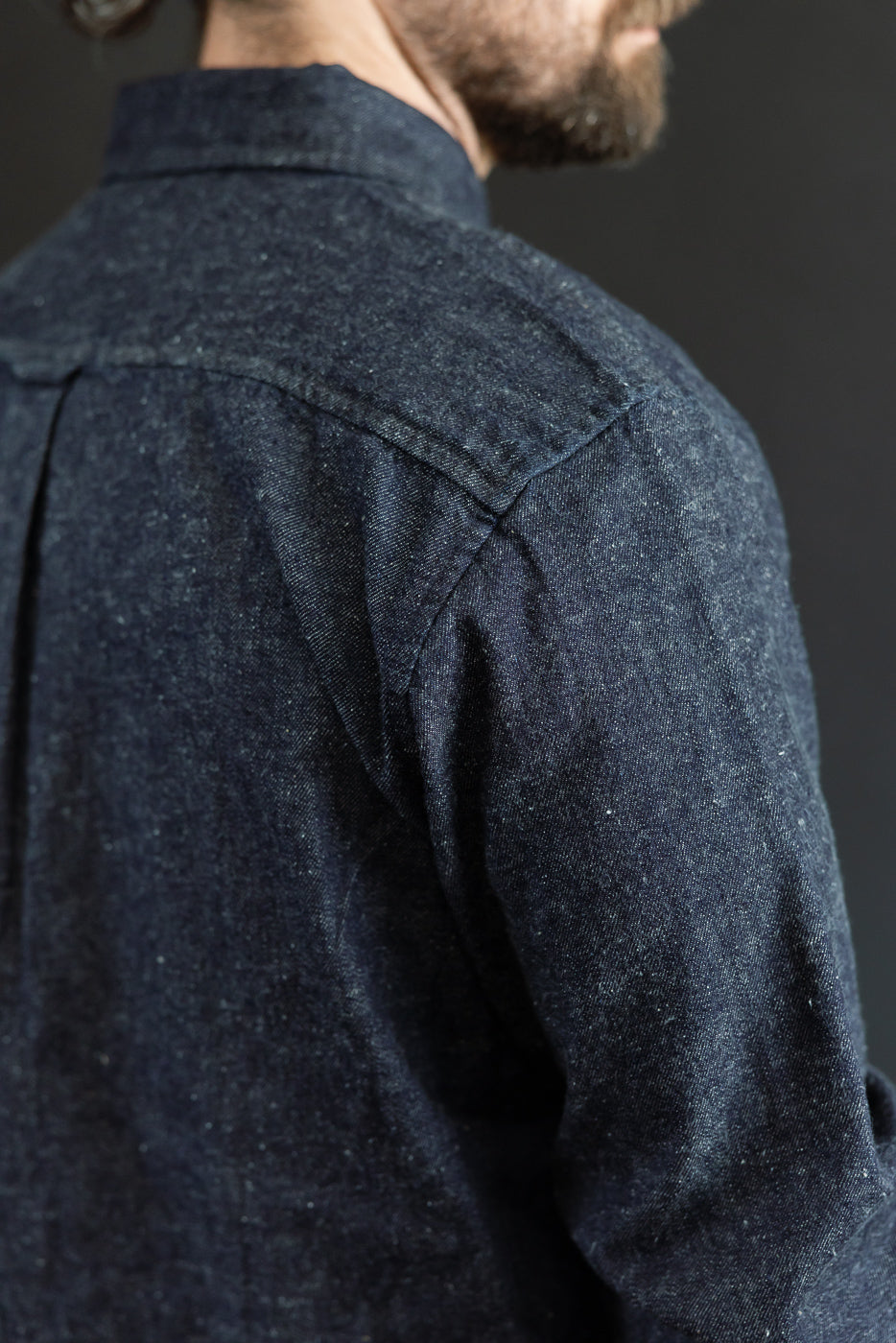 Close-up back view of a dark indigo denim shirt showing shoulder seam and fabric texture.