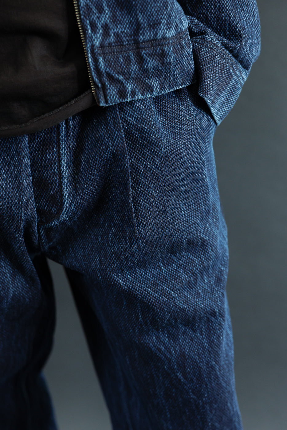 Close-up of the front waist and hip area of blue denim trousers, showing heavy fabric texture.