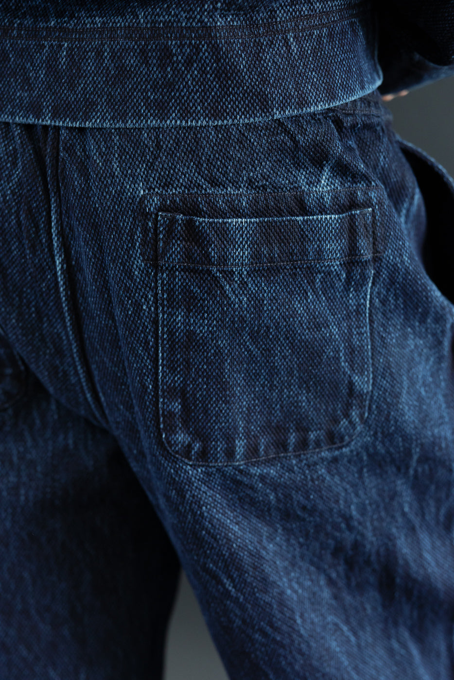 Close-up back view of dark indigo denim jeans showing the rear pocket and fabric texture.