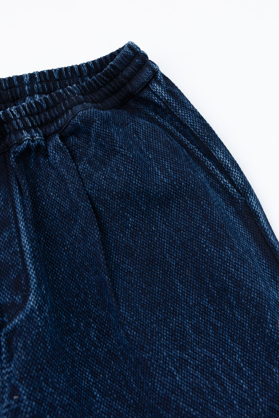 Close-up of the front waistband and drawstring detail on dark indigo textured lounge pants.