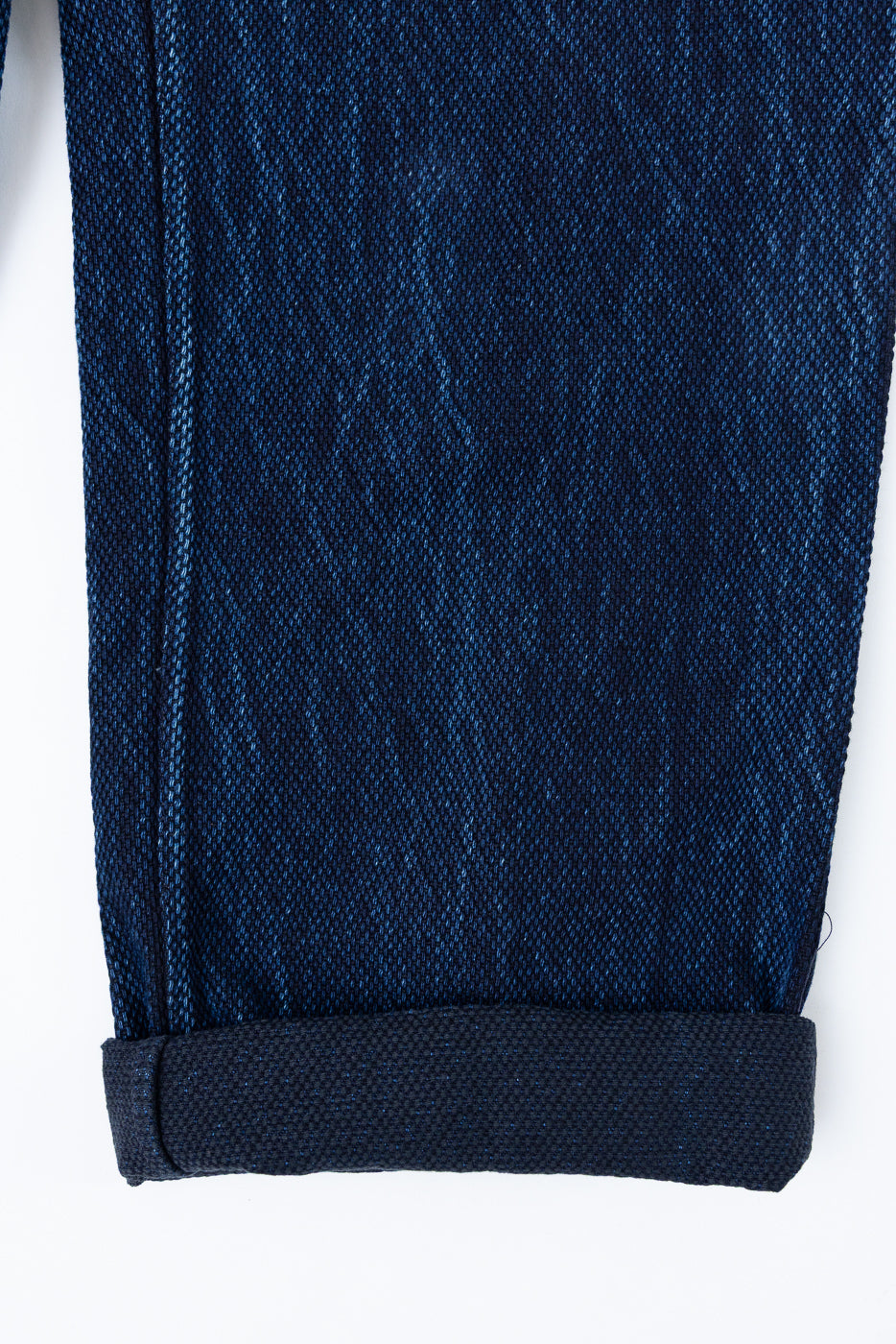 Close-up of the rolled hem and textured indigo denim fabric on the bottom of a pair of jeans.
