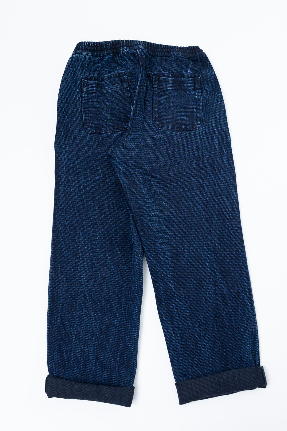 Back view flat lay of dark wash denim trousers with rear patch pockets and cuffed hems.