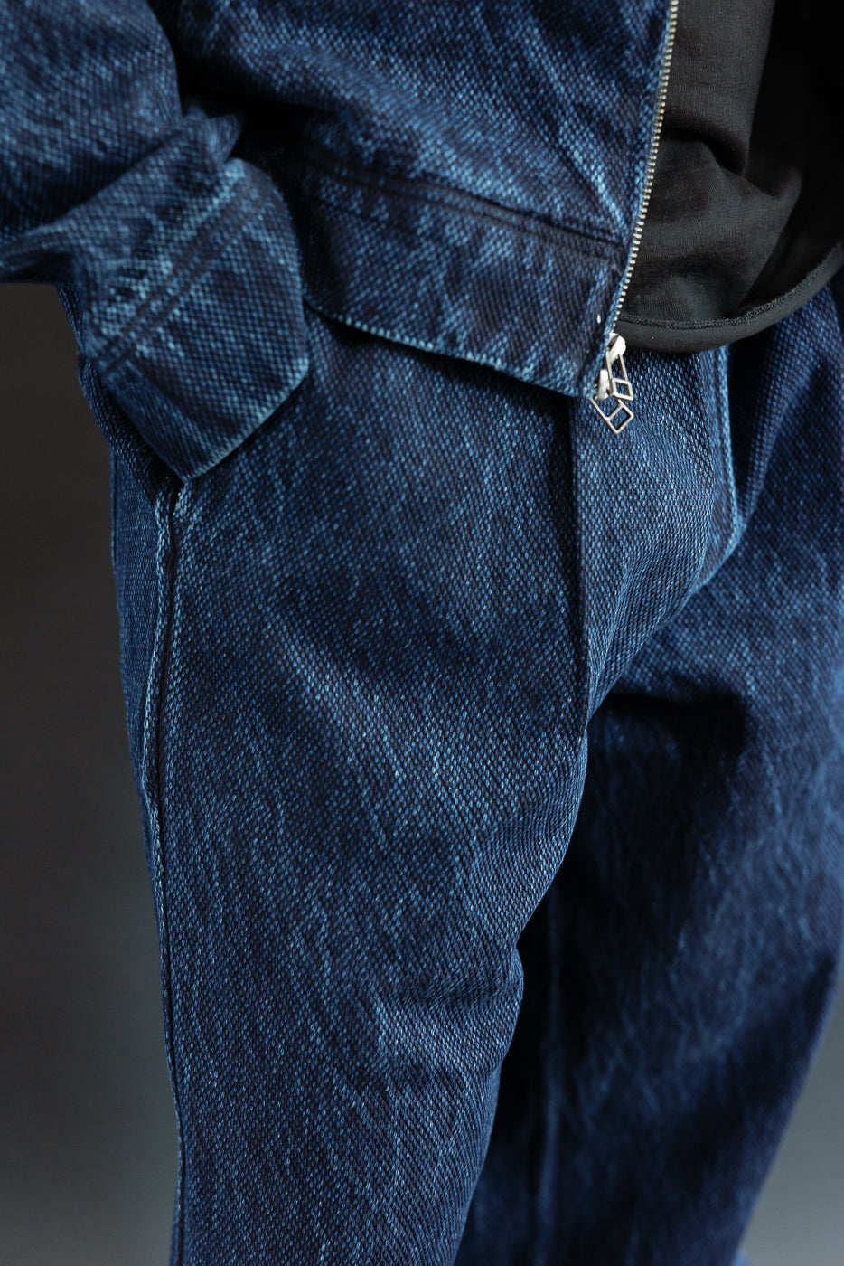 Close-up of the front waist and zipper detail on blue washed denim trousers.