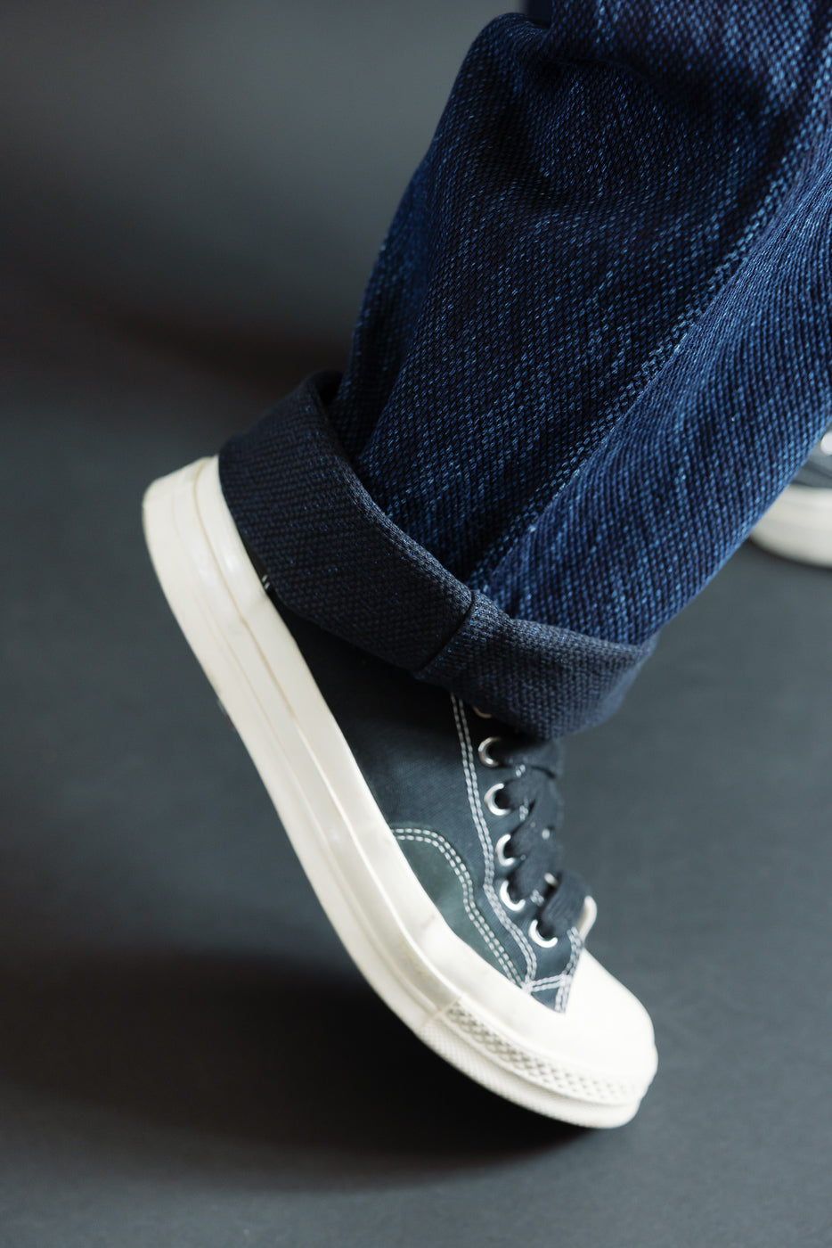 Close-up of the bottom hem and cuffed leg of dark indigo selvedge denim jeans with white sneakers.