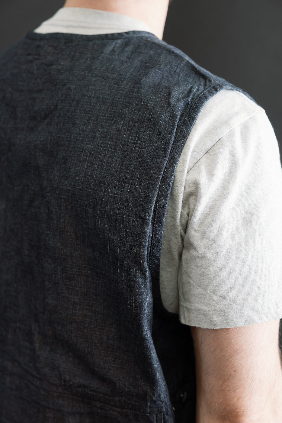 Close-up of male model's back wearing indigo ripstop field vest, textured fabric visible, 5'9