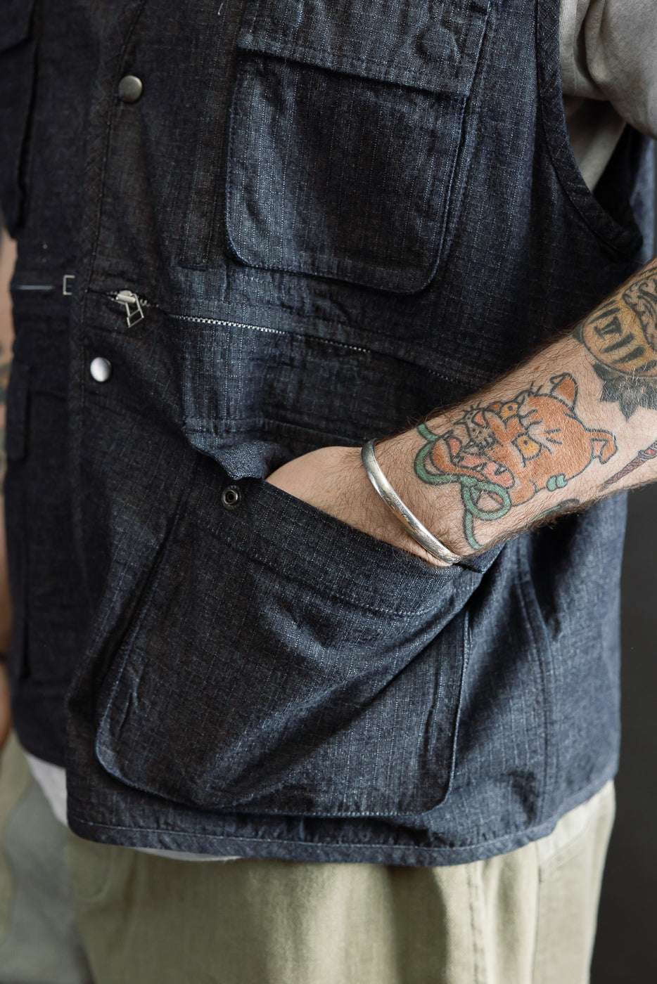 Close-up of male model's right side wearing indigo ripstop field vest, highlighting snap pockets, zipper detail, and textured fabric. Model is 5'9