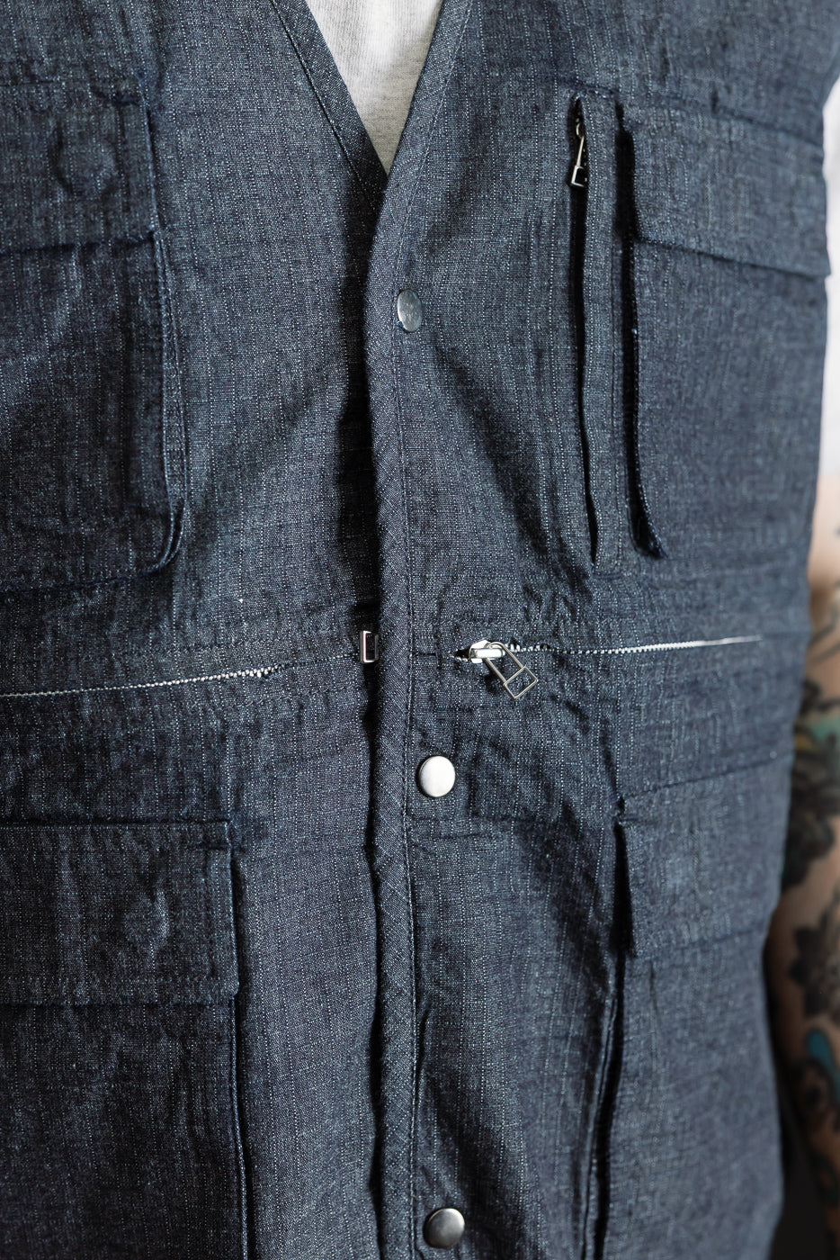 Close-up front view of indigo ripstop field vest on male model, showing pockets, zippers, and snap buttons, model is 5'9