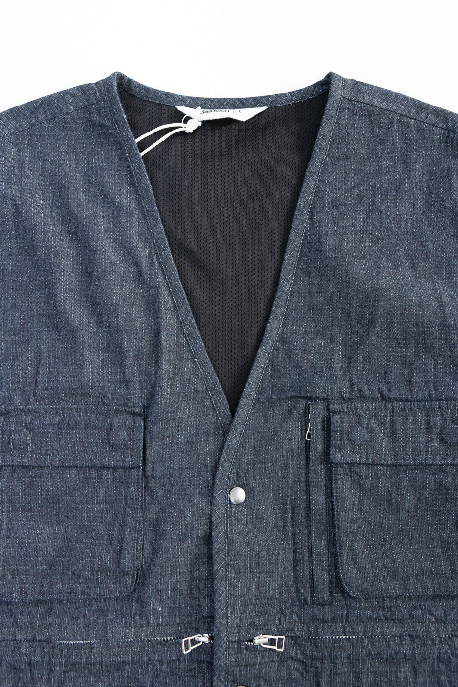 Close-up front view of indigo ripstop field vest showing chest pockets, snap button, and zipper details.