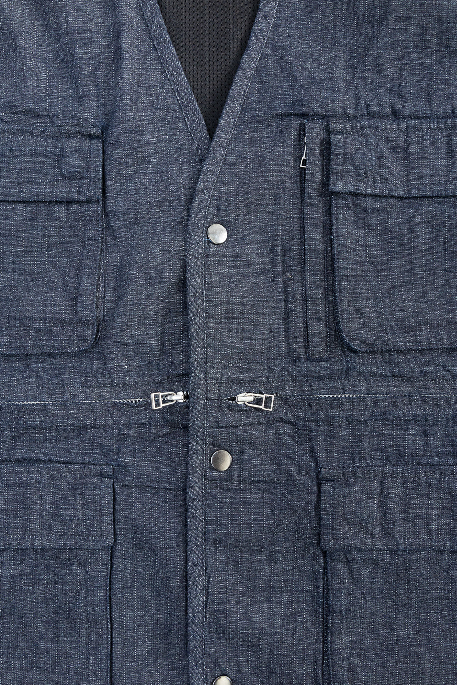 Close-up of front midsection of indigo ripstop field vest, showing snap buttons, zippers, and pockets.