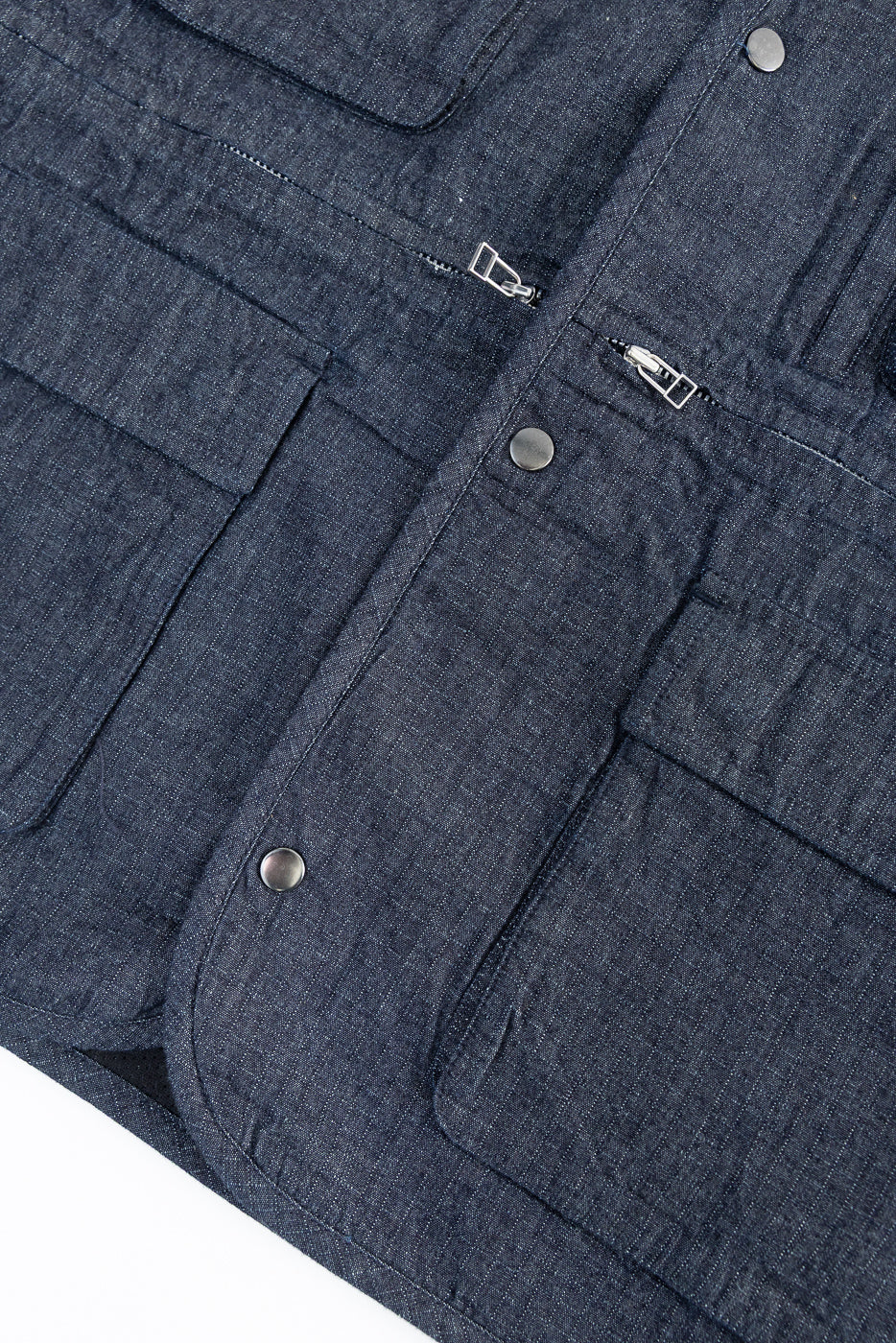 Close-up of front indigo ripstop field vest showing snap buttons, front zipper, and textured fabric.