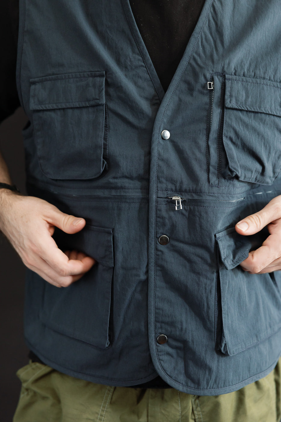 Close-up front view of a navy utility vest showing large cargo pockets and snap button closure.