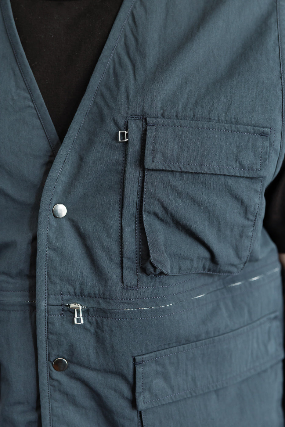 Close-up front view of a navy utility vest showing pocket details and silver metal hardware.