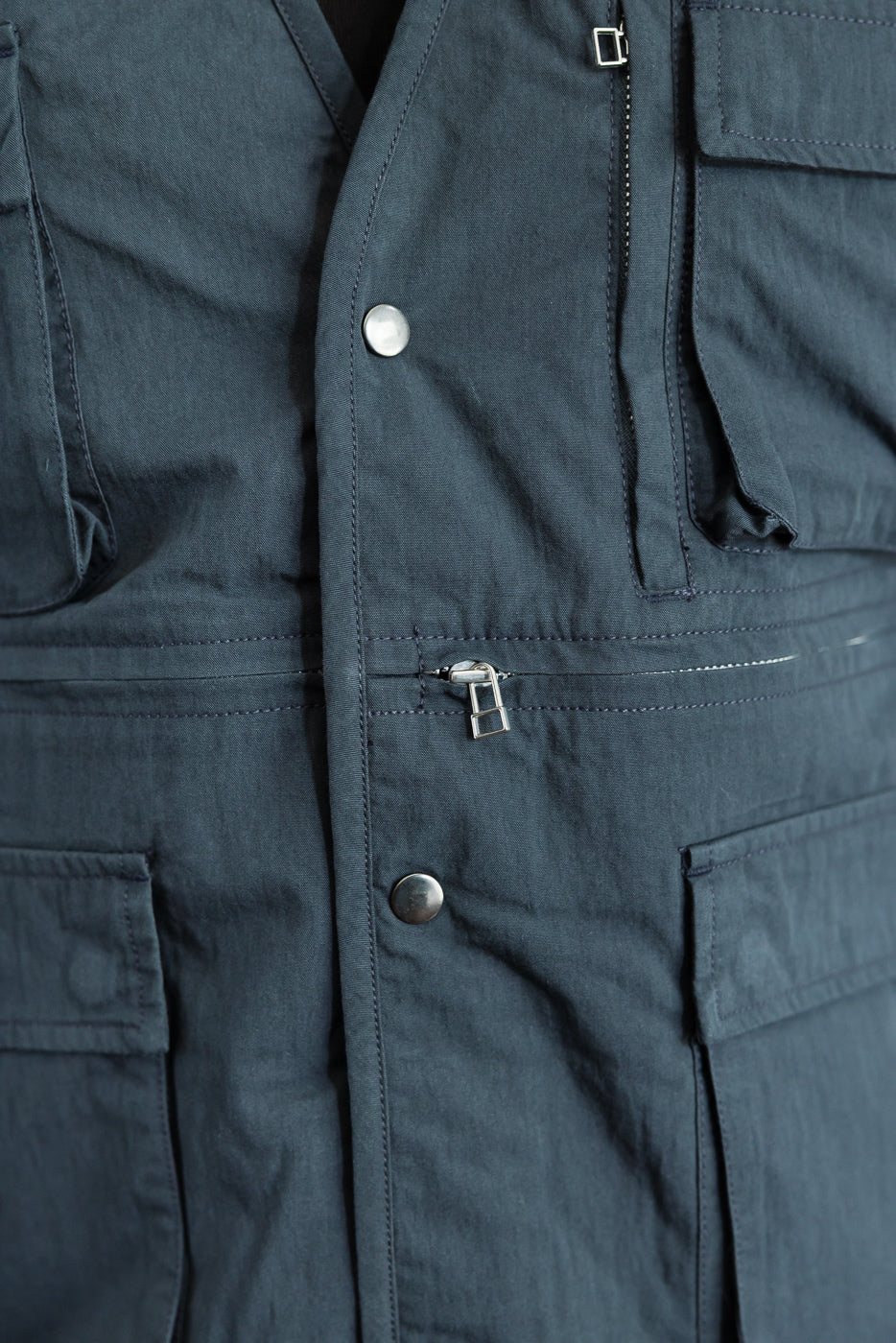 Close-up front view of dark navy utility garment showing zipper details and metal snap buttons.